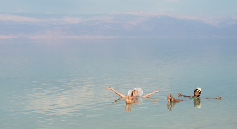 Lovely girls floating in salty water of Dead Sea and with Arms outstretched . Unusual buoyancy caused by high salinity.